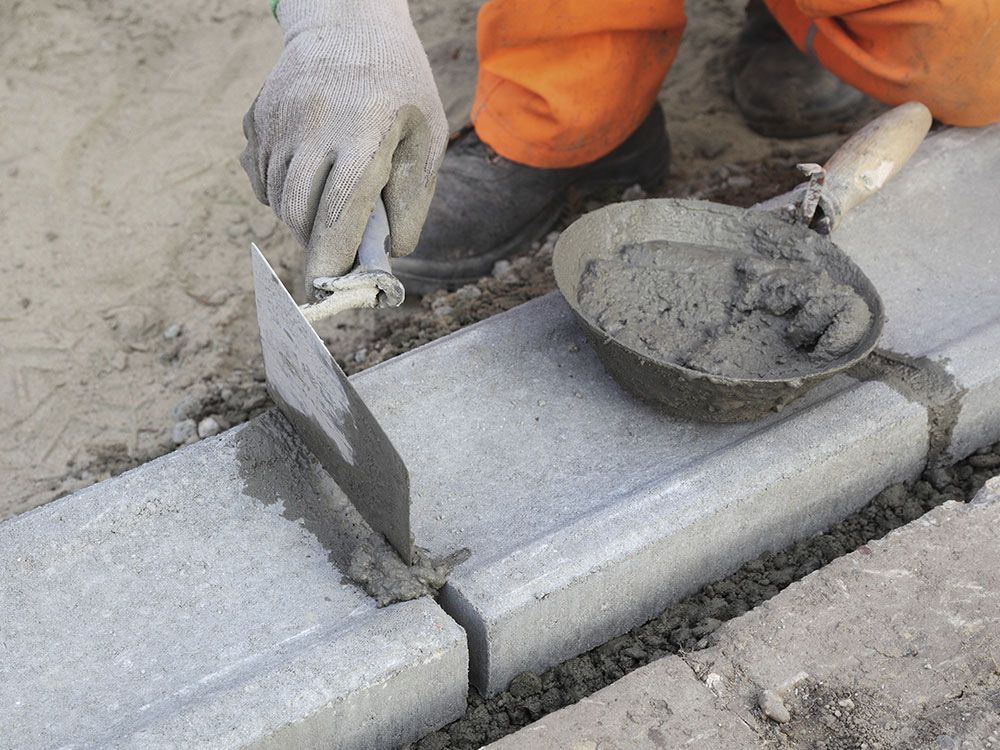 a person is using a trowel to spread concrete on a sidewalk
