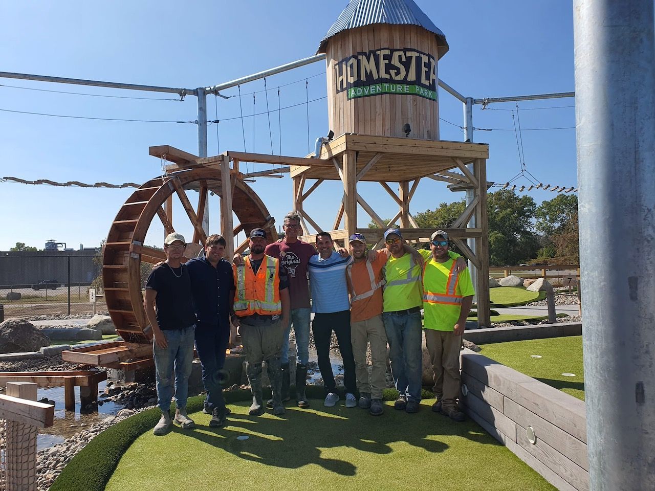 A group of men standing in front of a water tower that says homestead