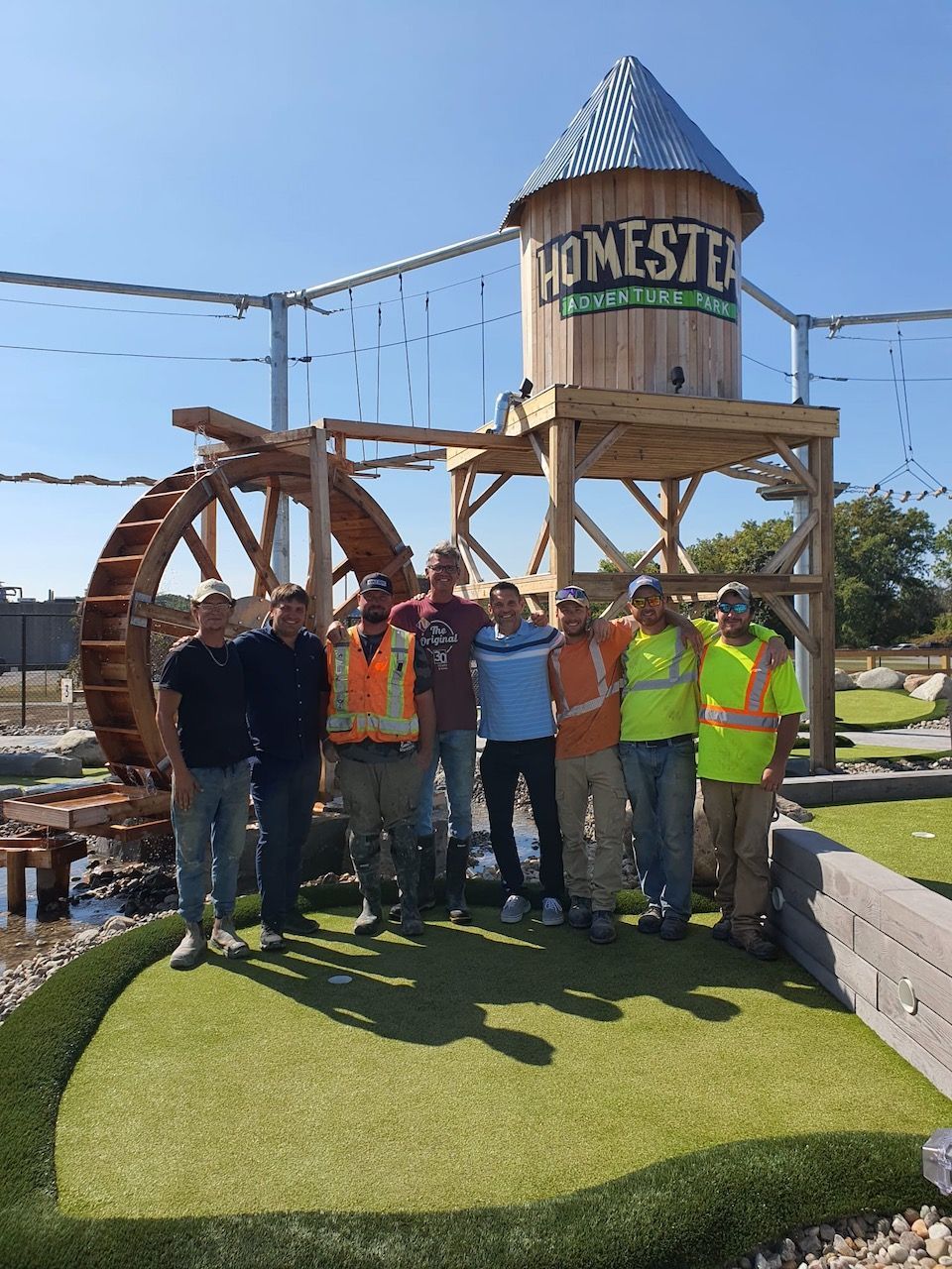 A group of men standing in front of a water tower that says homeste