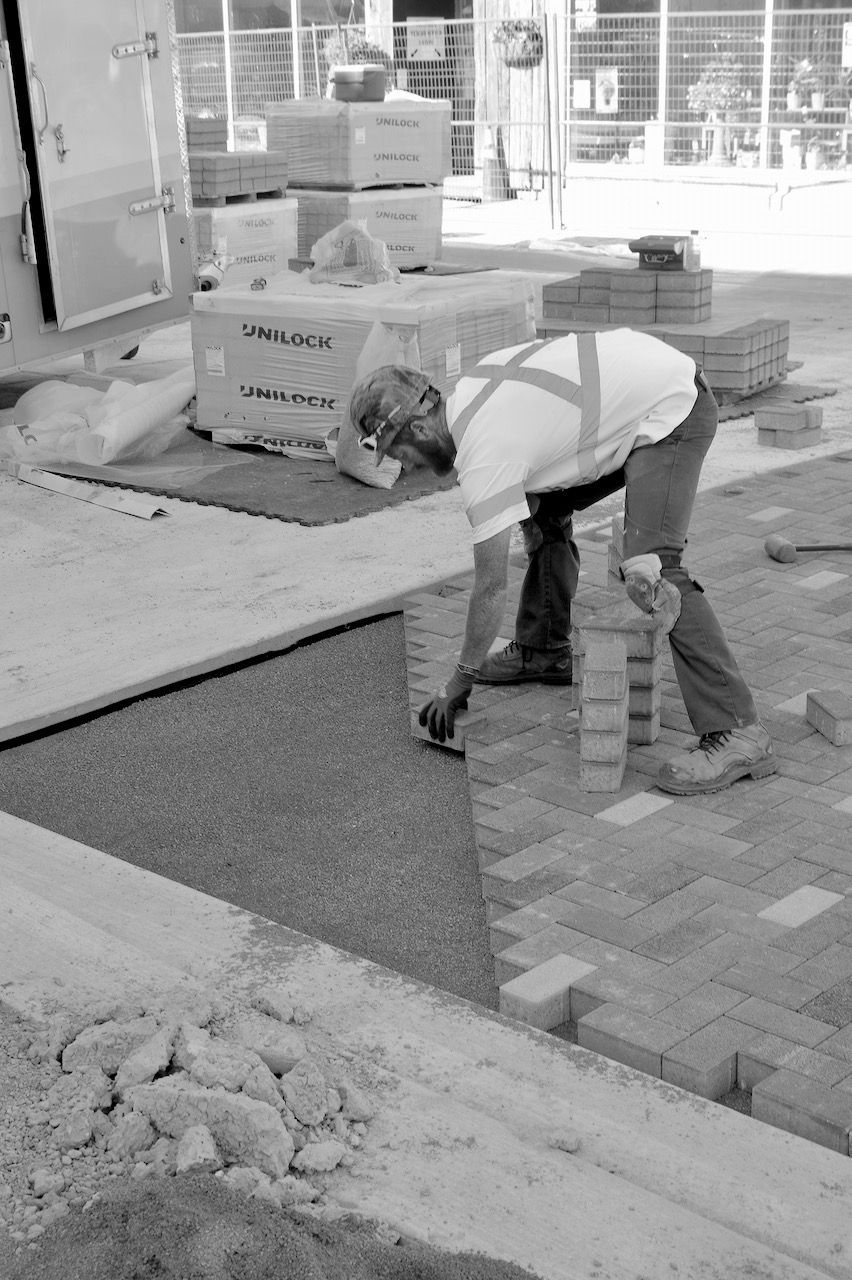 A man is laying bricks on a sidewalk in a black and white photo.