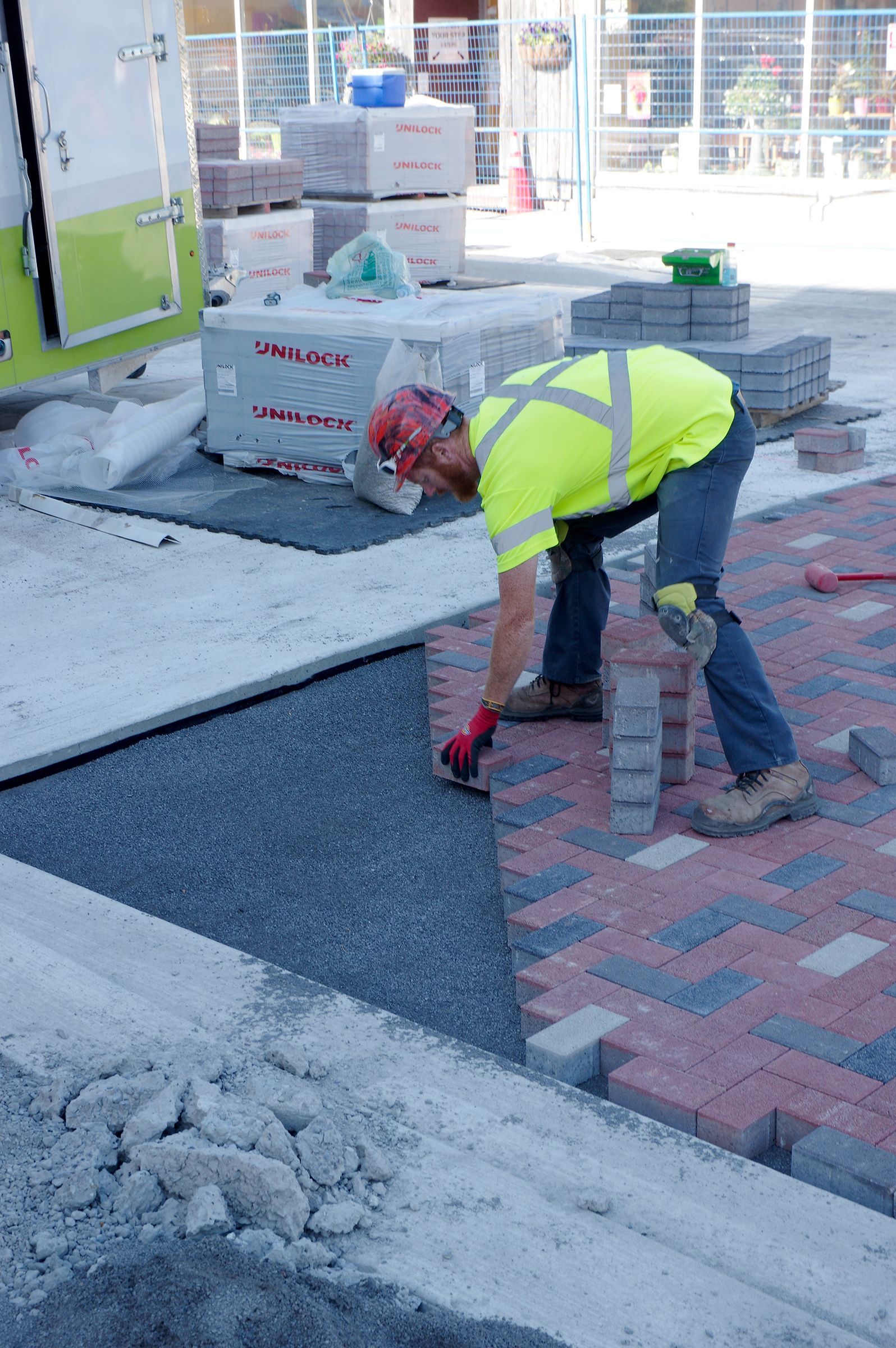 A construction worker is laying bricks on a sidewalk.