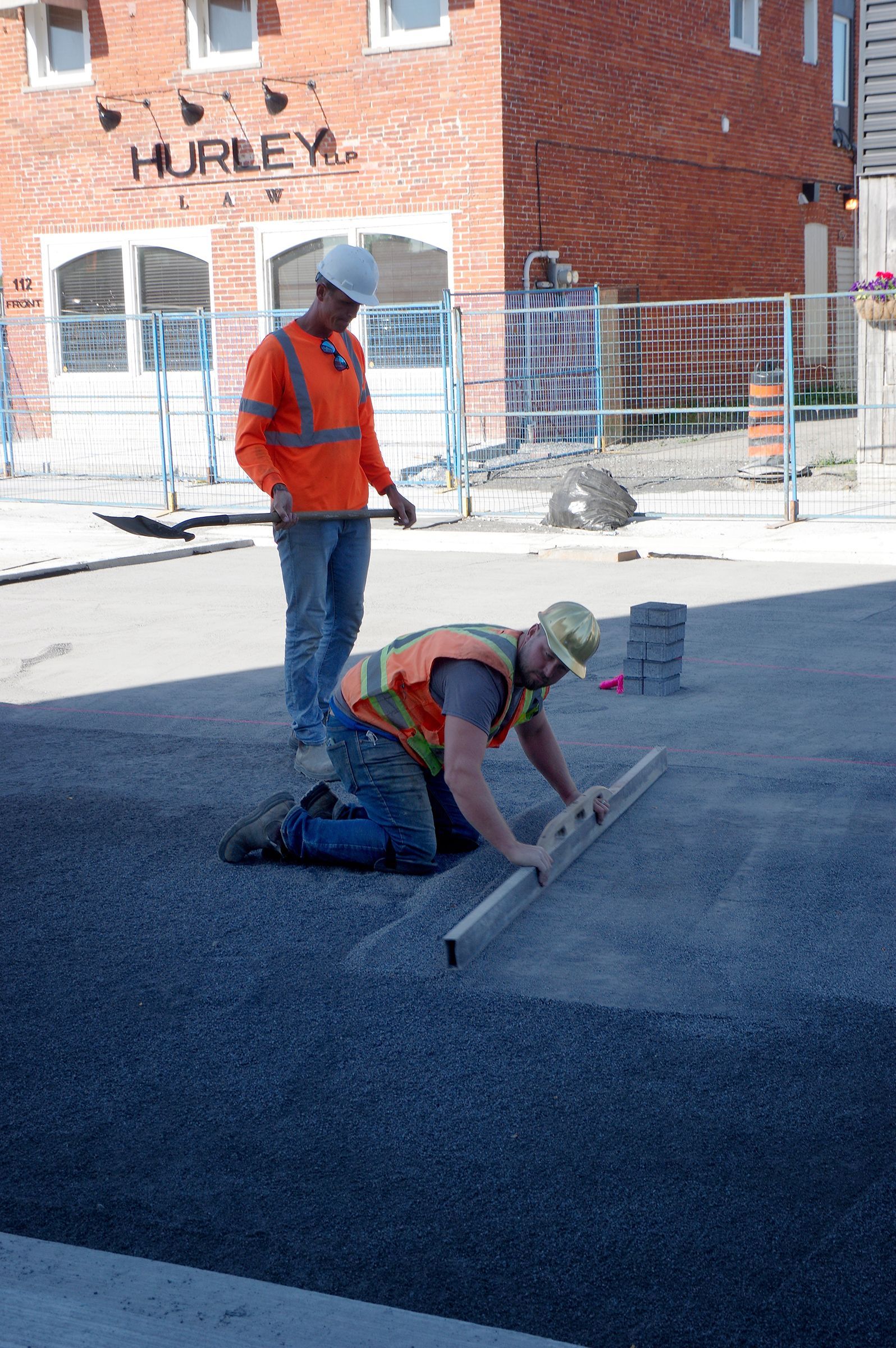 Two construction workers are working on a road in front of a hurley building
