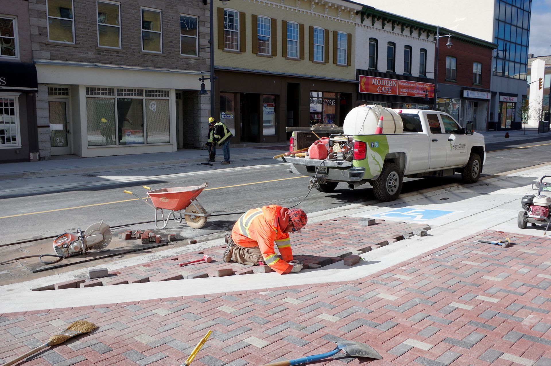 A man is working on a brick sidewalk in front of a truck.