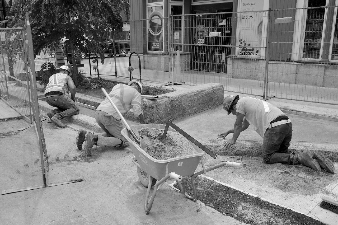 A group of construction workers are working on a sidewalk.
