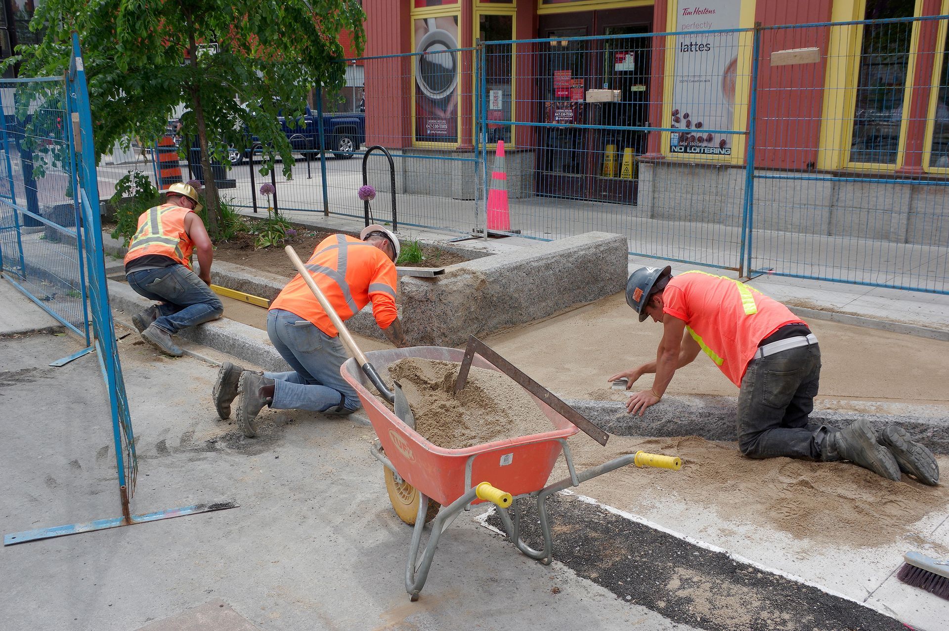 Three construction workers are working on a sidewalk in front of a building