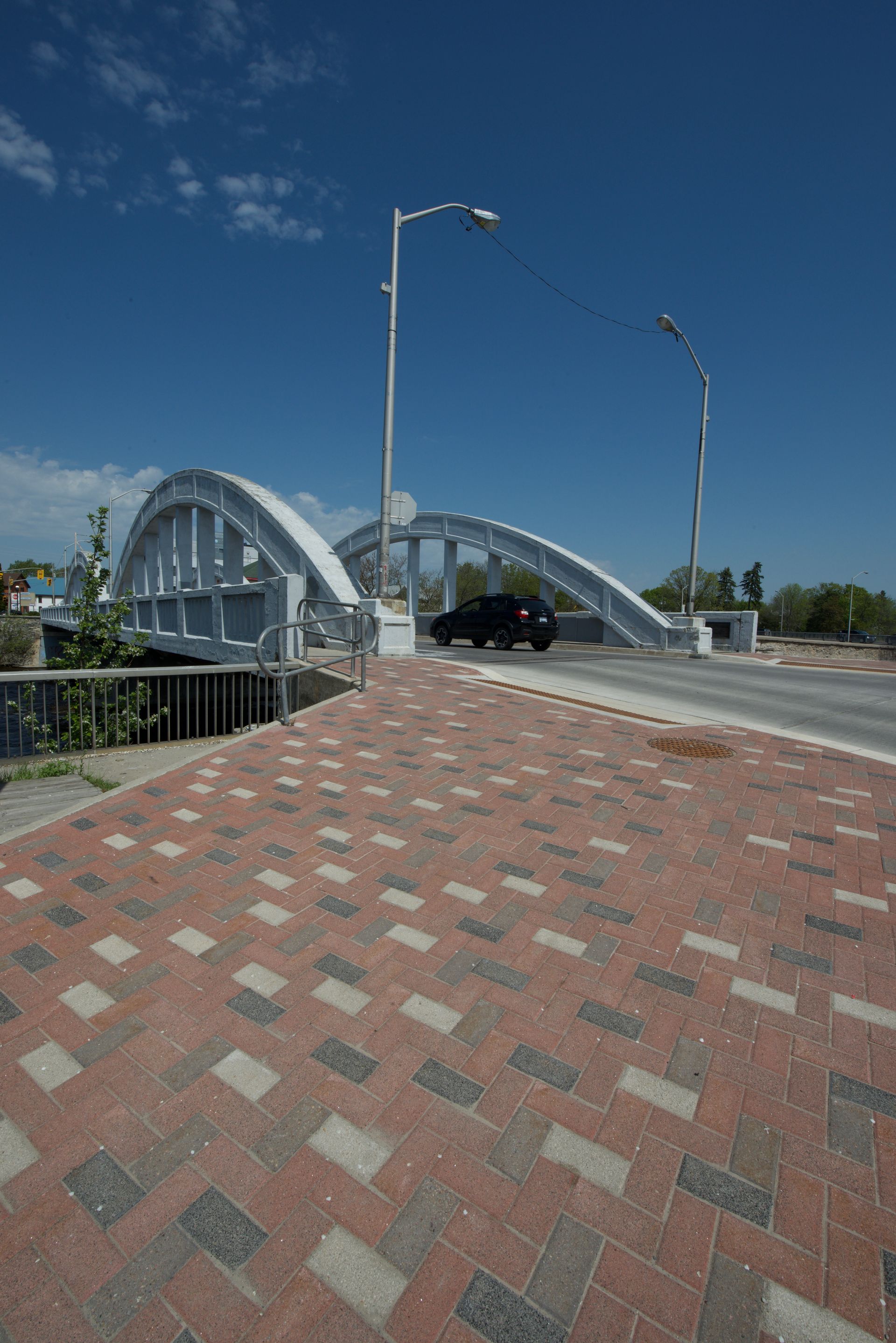 A car is driving under a bridge on a brick walkway.
