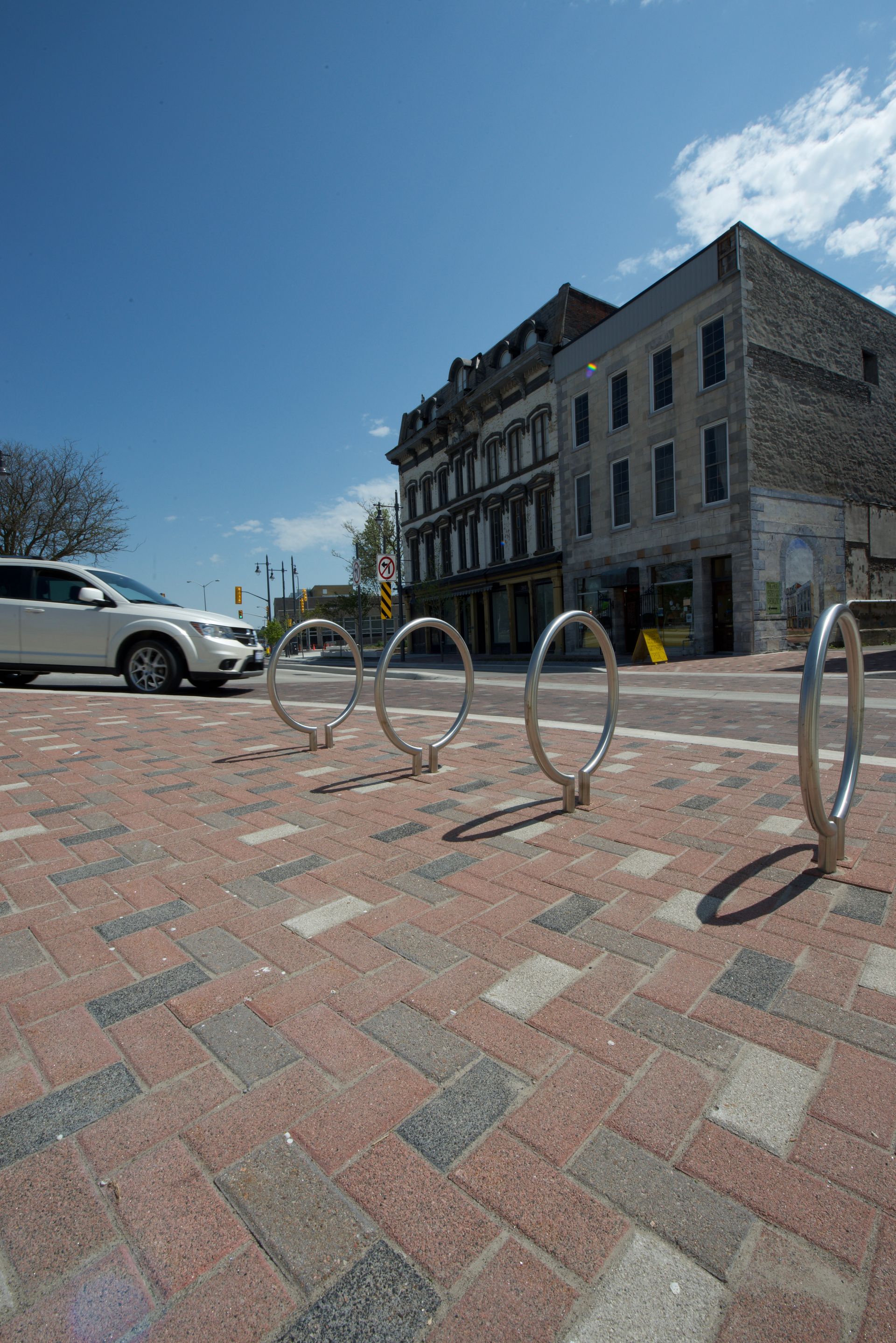 A white car is parked on the side of the road next to a row of bike racks.
