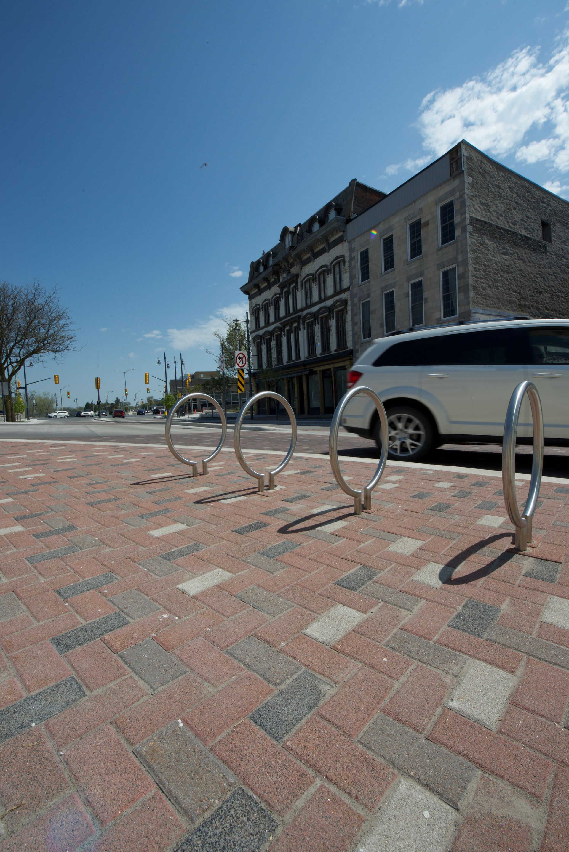 A white suv is parked on the side of the road next to a row of bike racks.