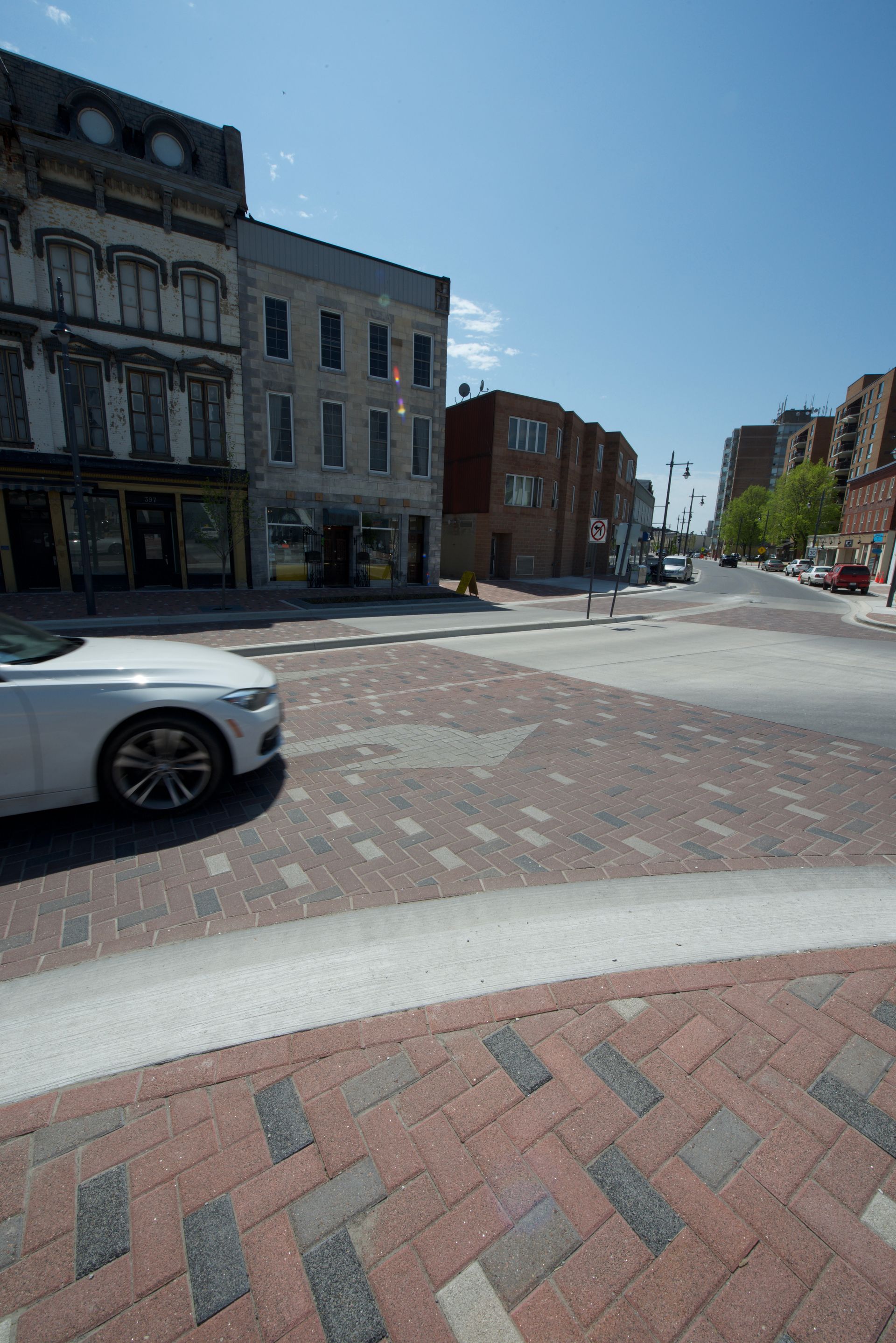 A white car is driving down a brick street in a city.