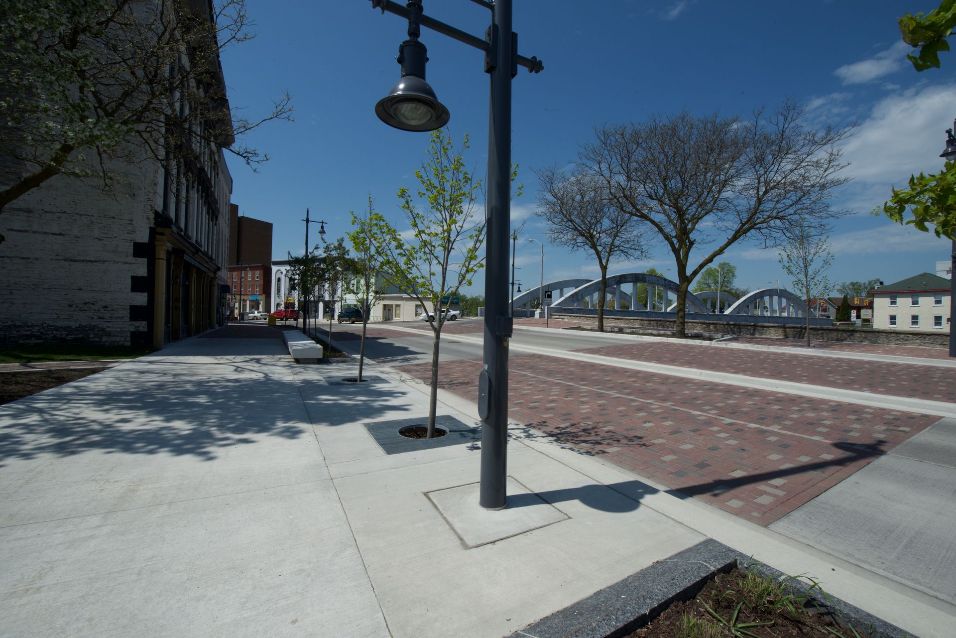 A brick sidewalk with a street light and a bridge in the background