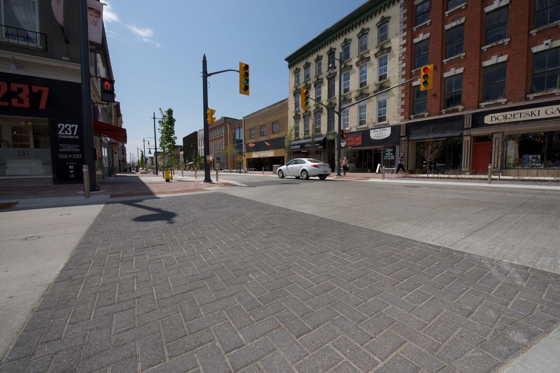 A white car is driving down a street in front of a building that says 237