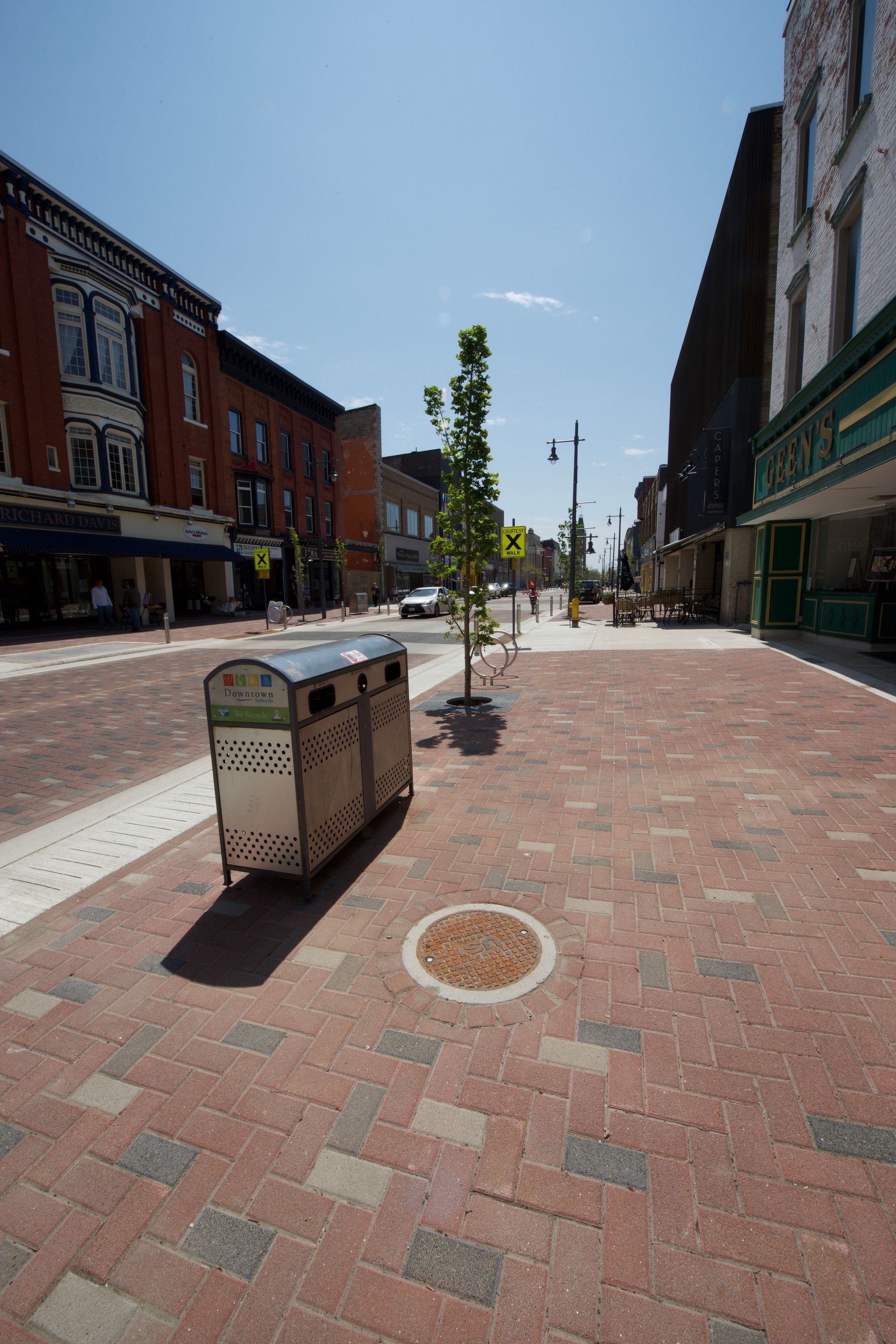 A brick sidewalk with a trash can in the middle of it
