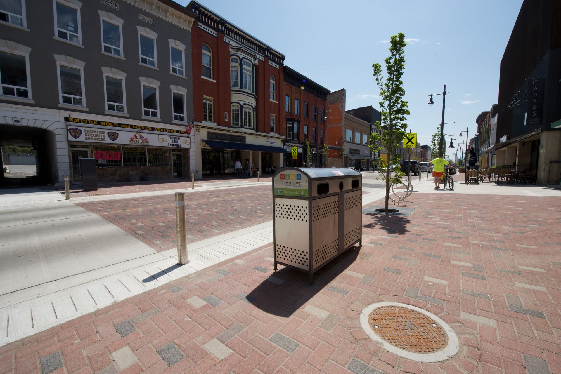 A trash can is sitting on a brick sidewalk in a city.