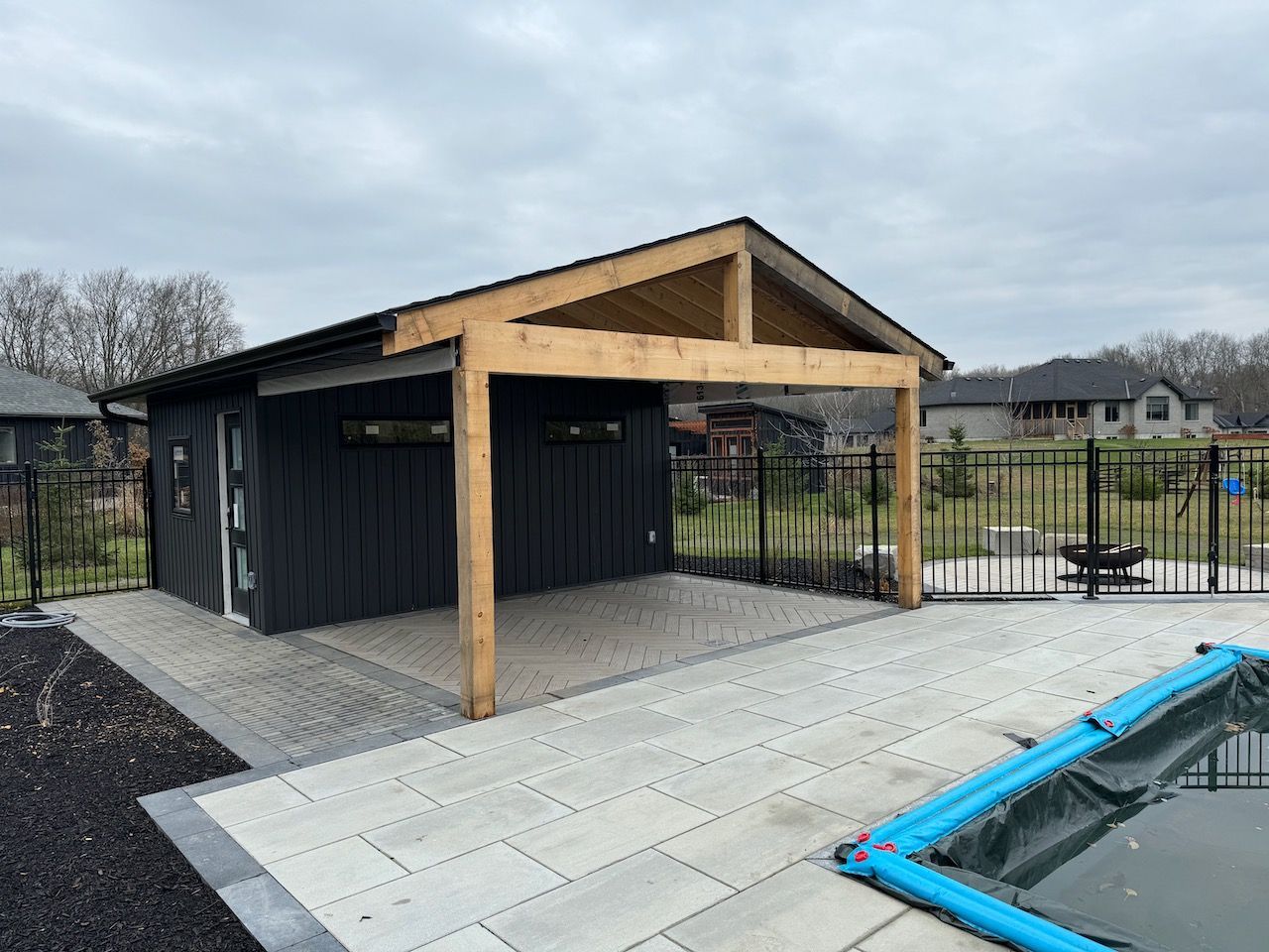A black garage with a wooden roof is next to a pool.