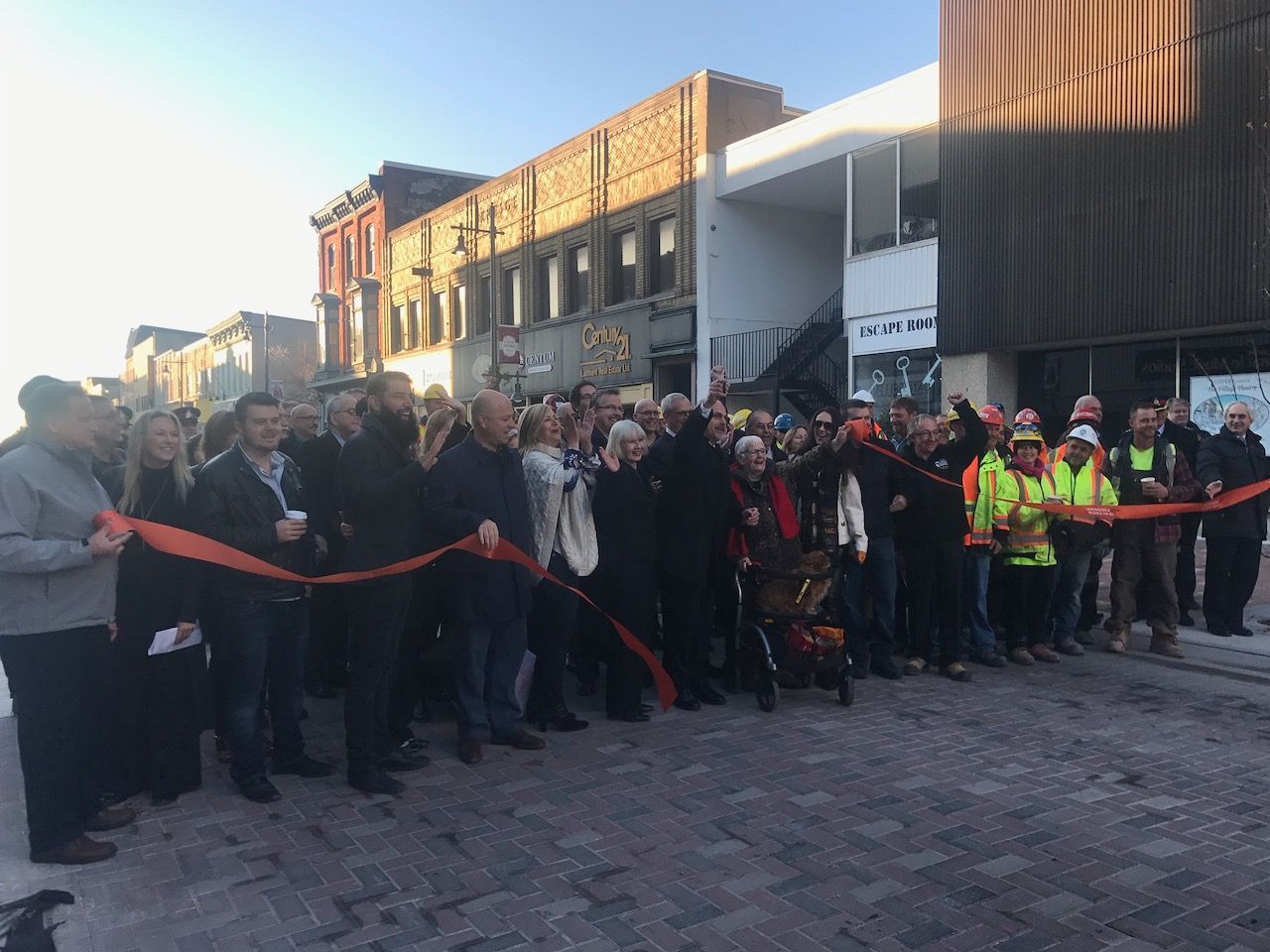 A large group of people are standing in front of a building cutting a red ribbon.