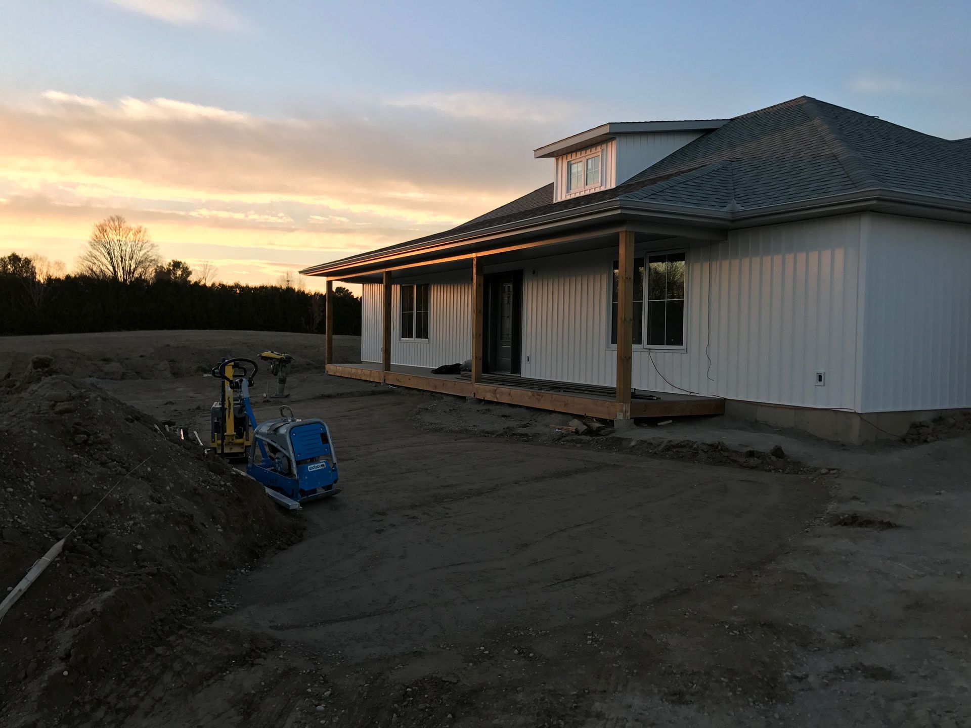 A white house with a porch is sitting in the middle of a dirt field.