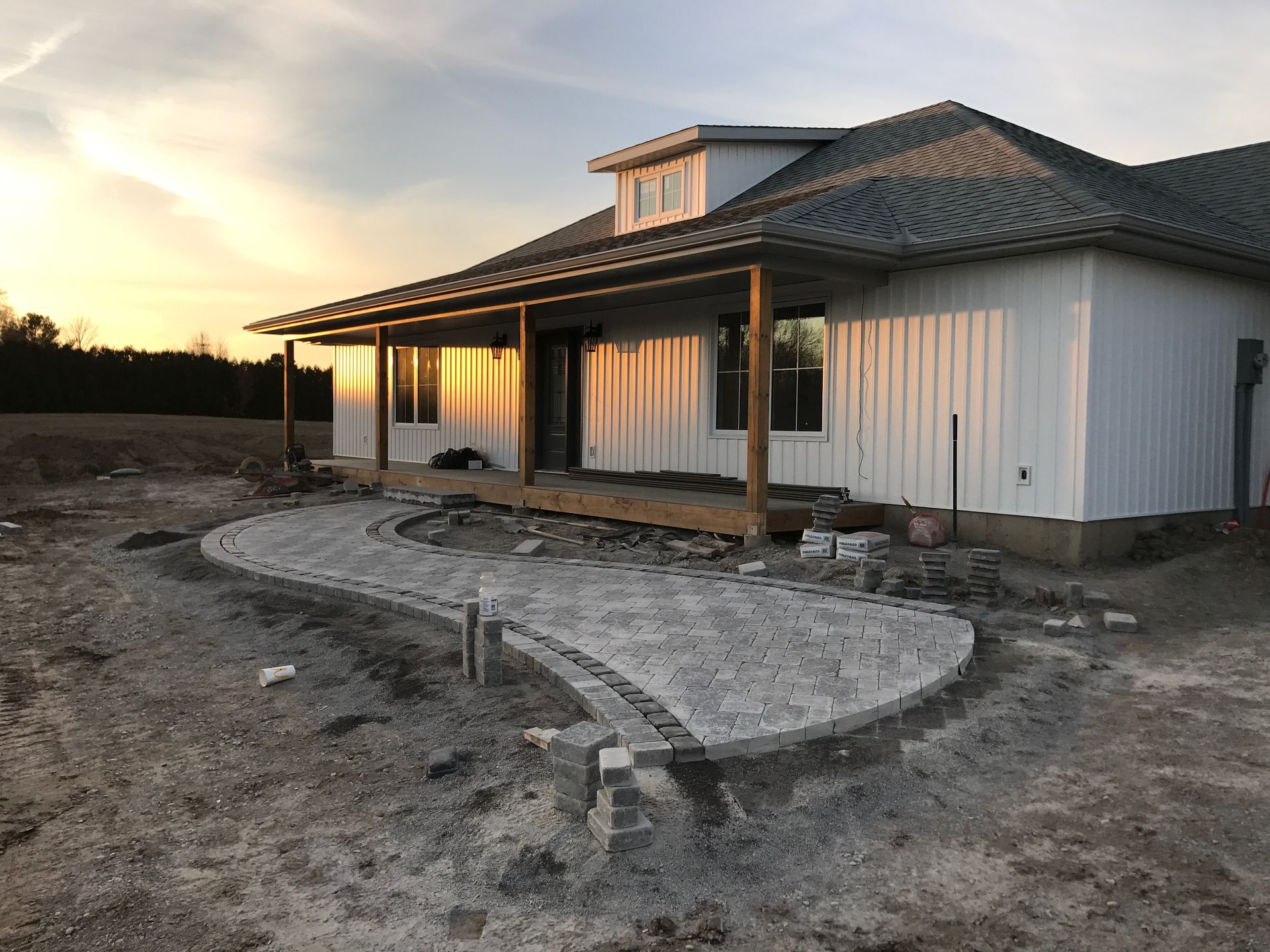 A white house with a porch is sitting in the middle of a dirt field.
