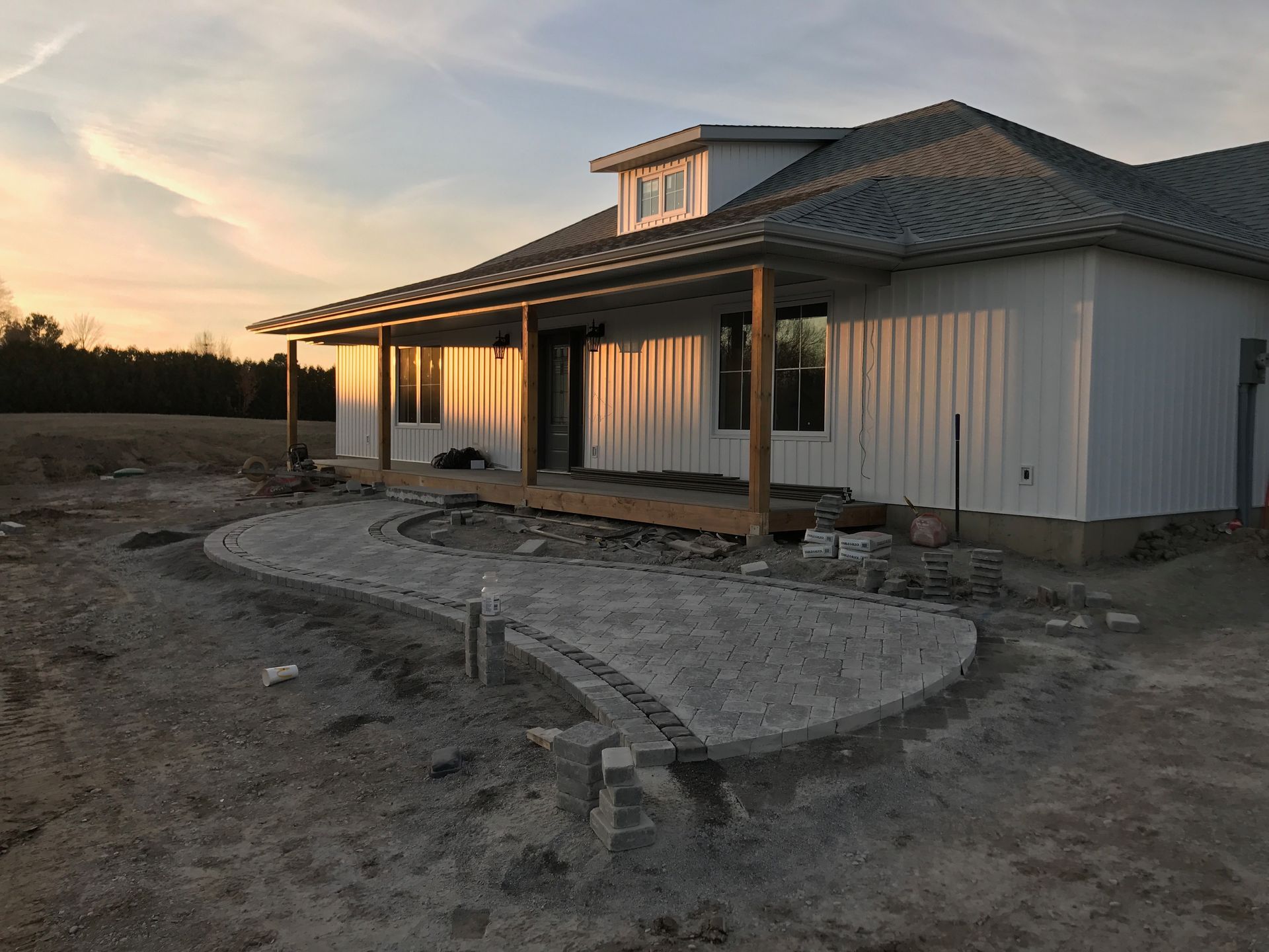 A white house with a porch is sitting in the middle of a dirt field.