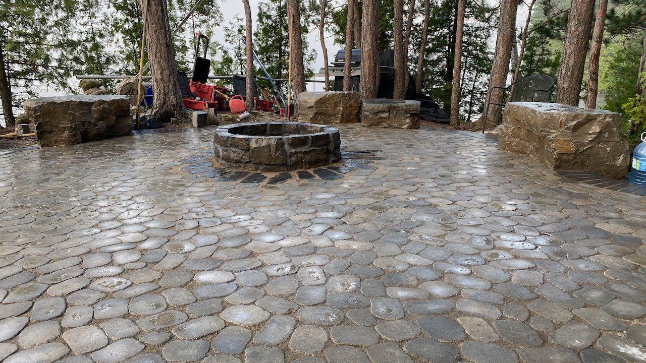 A stone patio with a fire pit in the middle of it surrounded by trees.