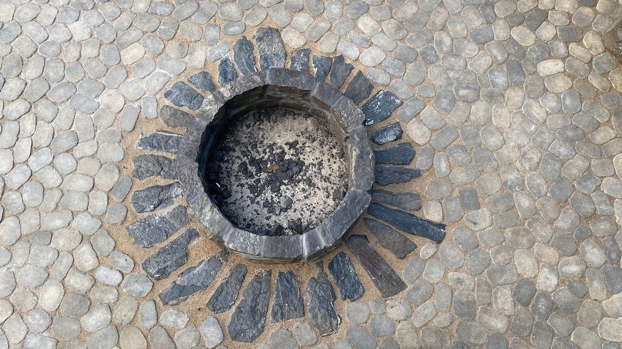 A stone ashtray is sitting in the middle of a stone pavement.