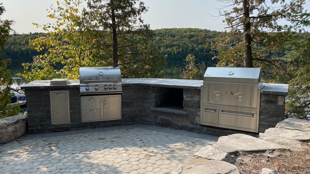 A large outdoor kitchen with a grill and oven is sitting next to a lake.