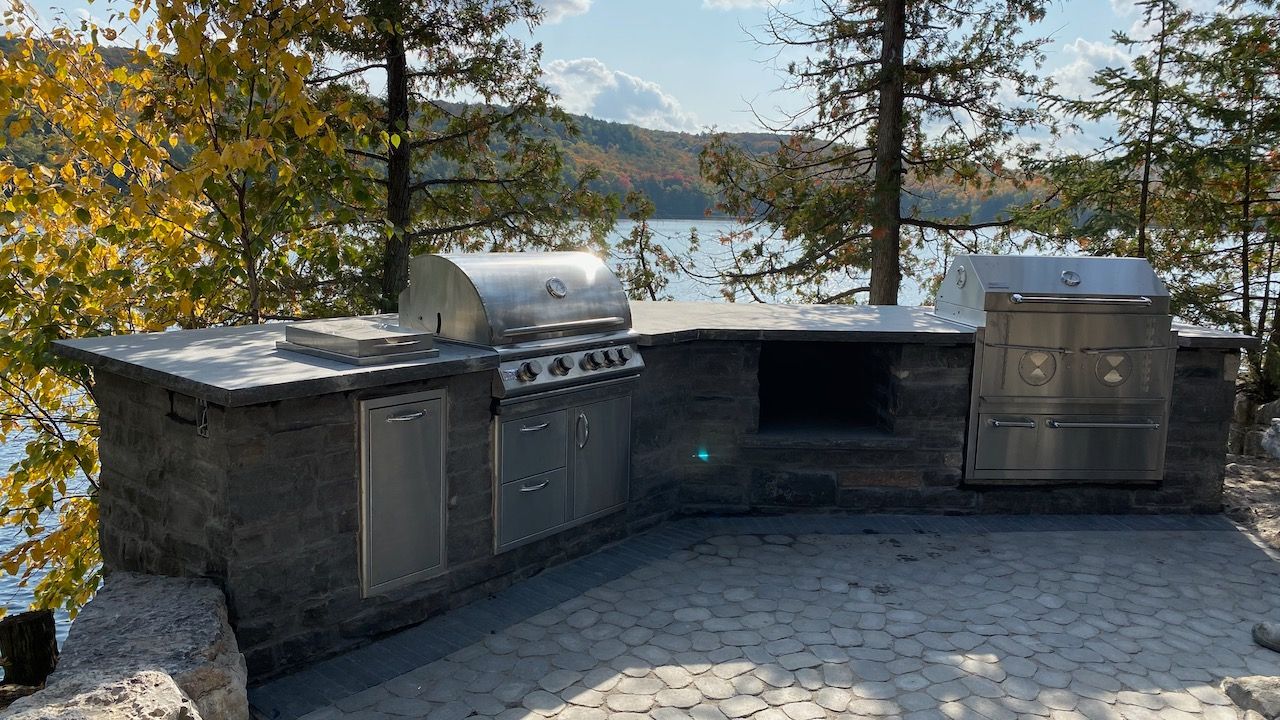 A large outdoor kitchen with a grill and a view of a lake.