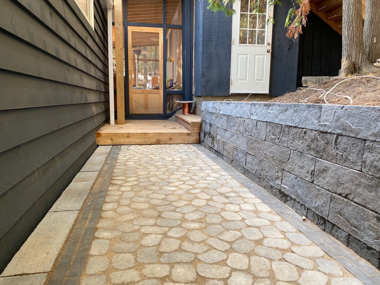 A stone walkway leading to a house with a black siding