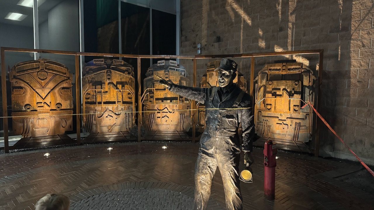 A statue of a man is standing in front of a wall of barrels.