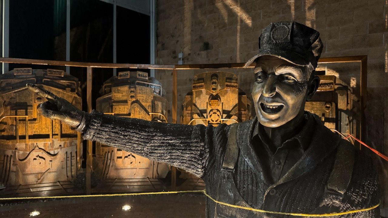 A statue of a man in a hat is standing in front of a building.