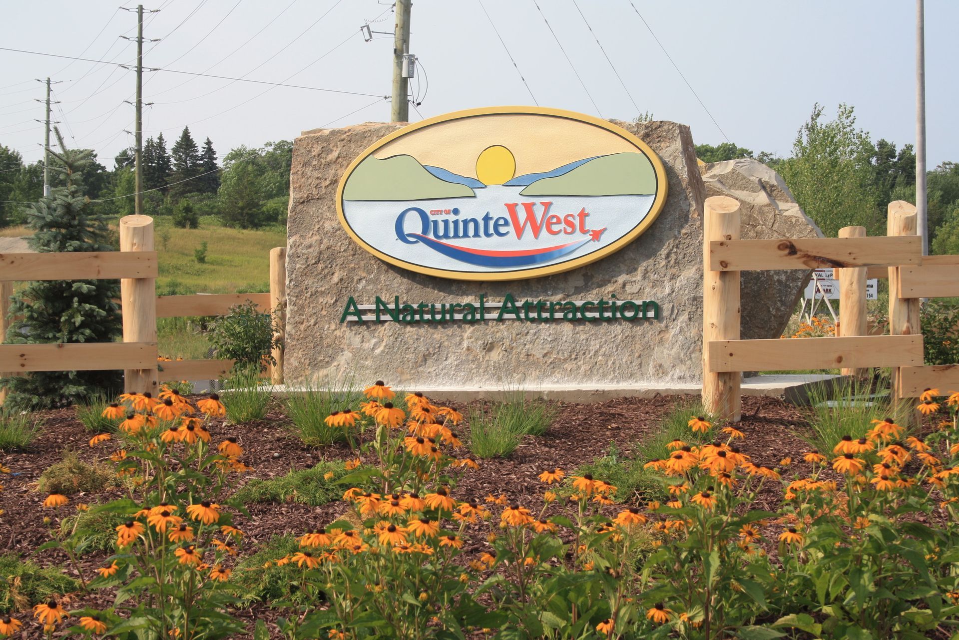 A sign for quinte west is surrounded by flowers