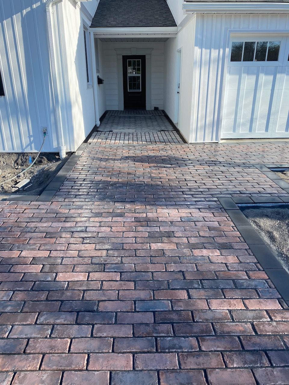 A brick driveway leading to a white house with a garage door.