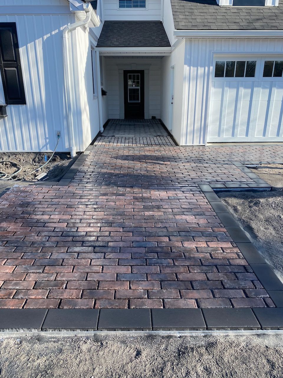 A brick walkway leading to the front door of a white house.