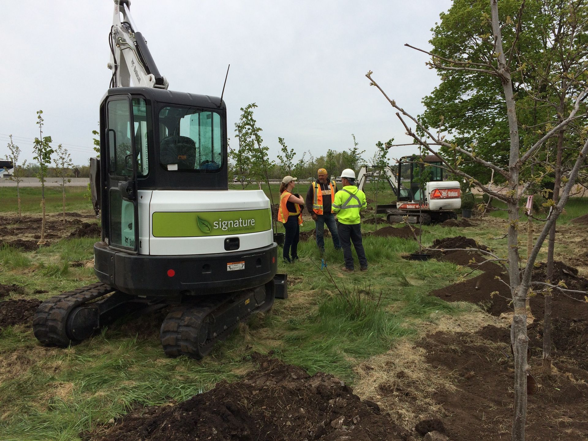 A group of construction workers are standing around a small excavator in a field.