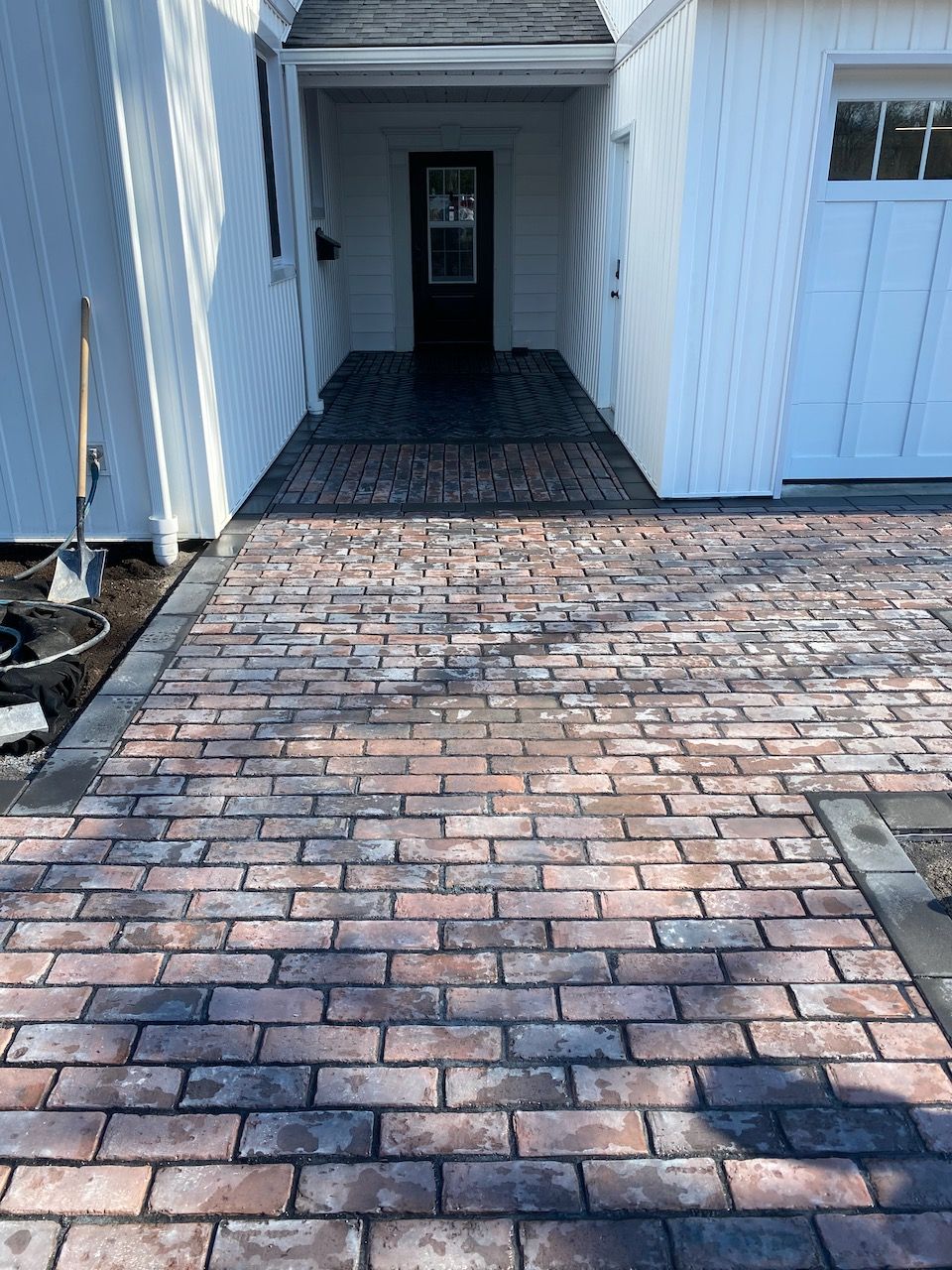 A brick driveway leading to a garage and a white house.