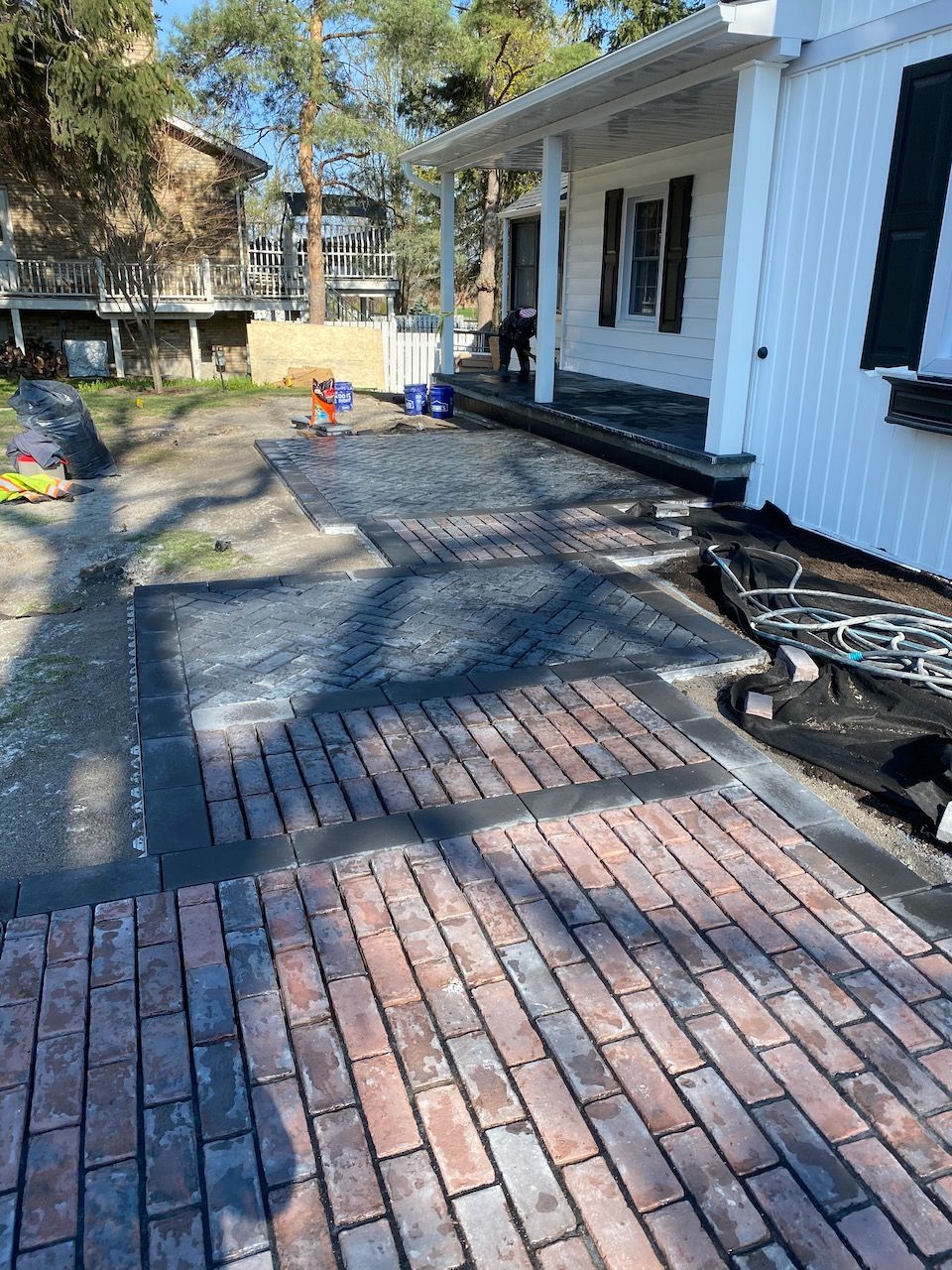 A brick driveway is being built in front of a white house.