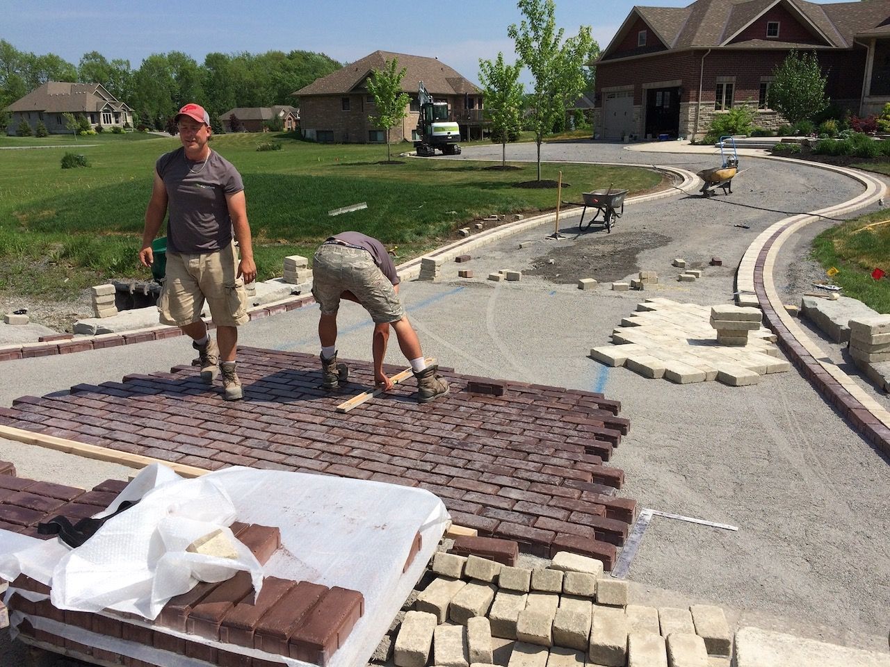 Two men are working on a driveway in front of a house.
