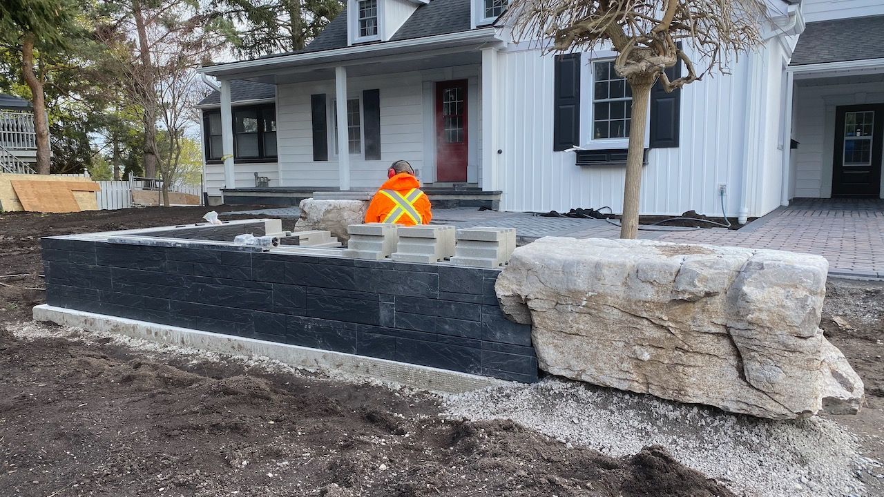 A large rock is sitting in front of a white house.