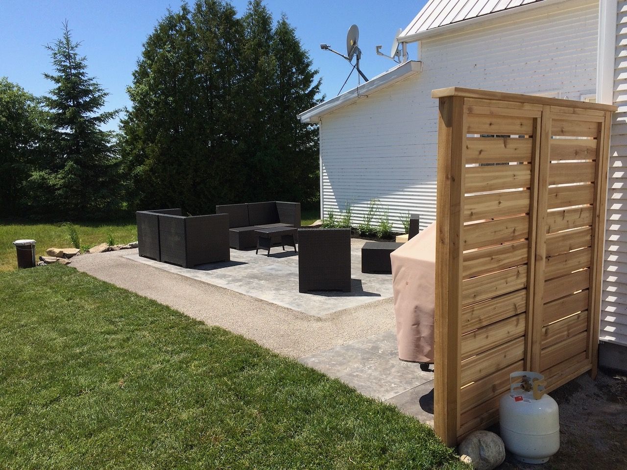 A wooden fence surrounds a patio with furniture and a grill.