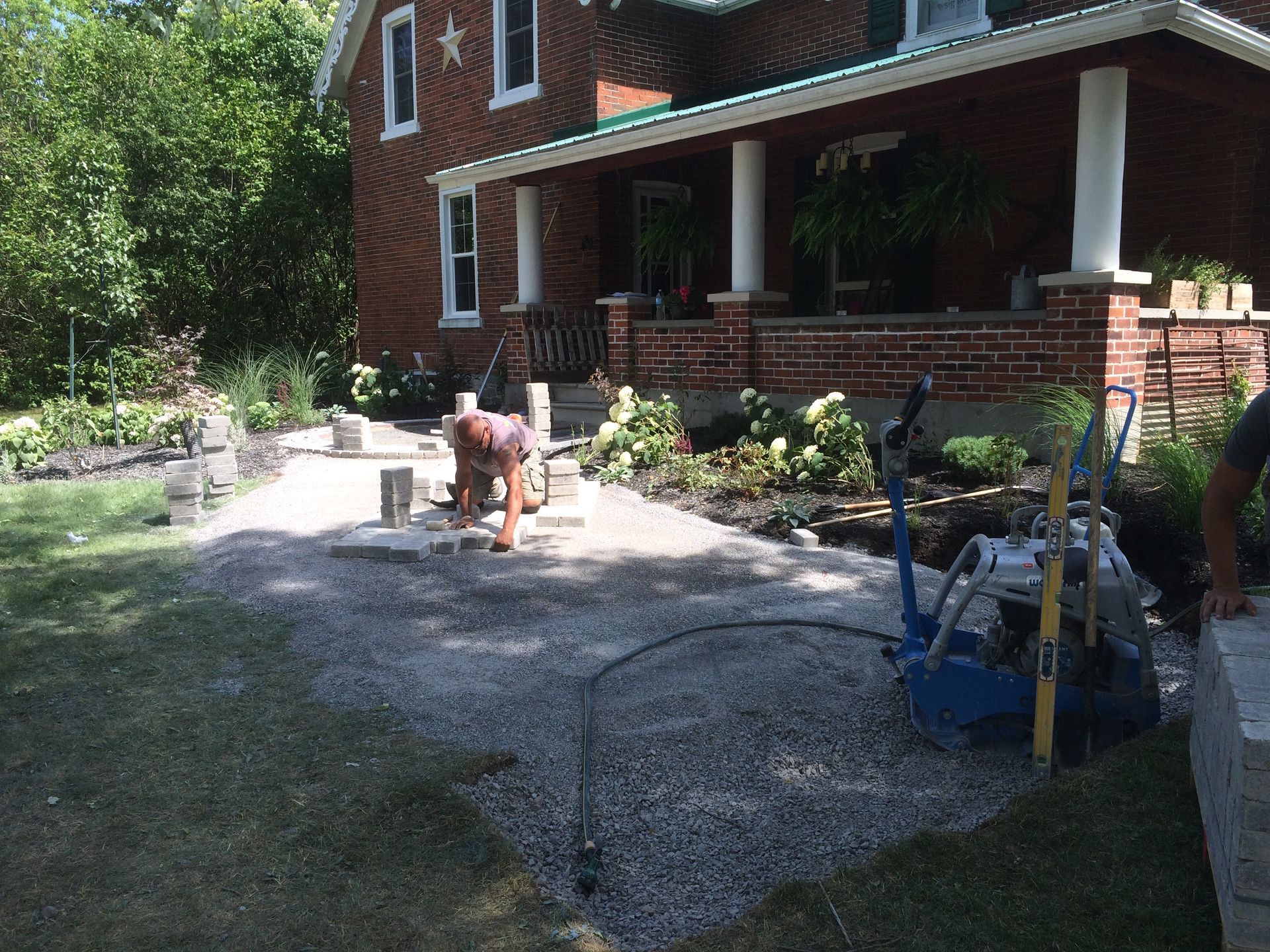 A man is working on a driveway in front of a brick house.