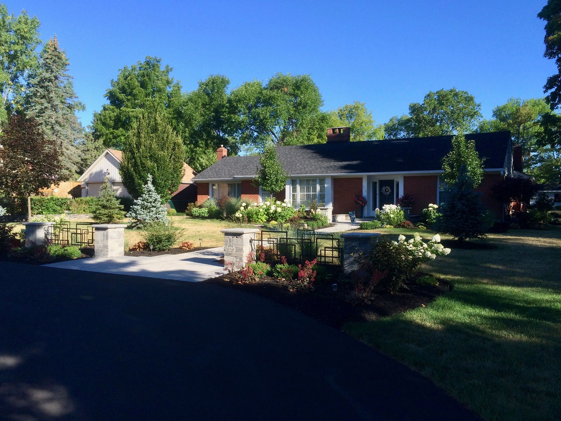 A brick house with a black roof is surrounded by trees and a driveway.
