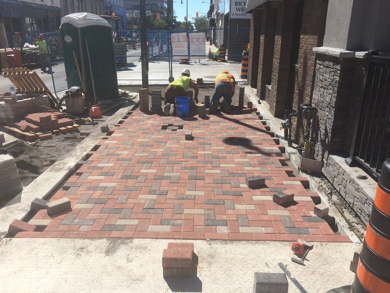 A group of construction workers are laying bricks on a sidewalk.