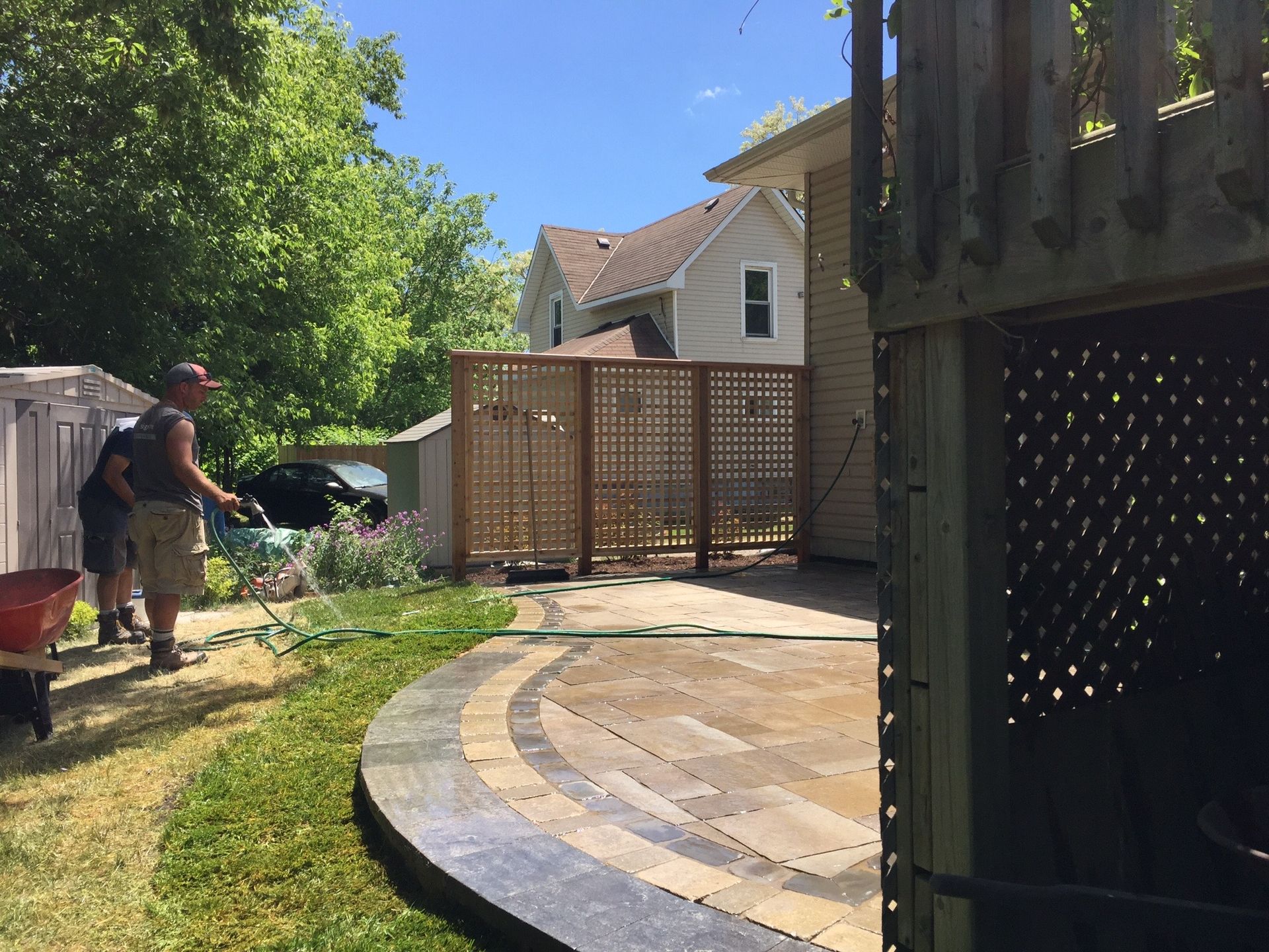 A man is watering a lawn with a hose in a backyard.
