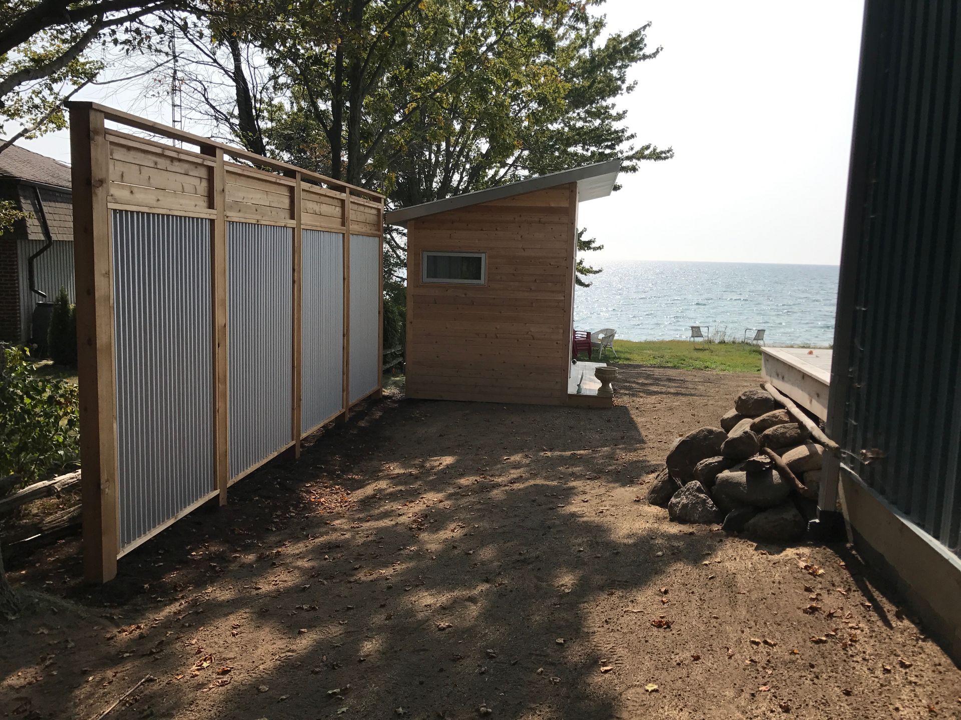A wooden shed is behind a fence with a view of the ocean