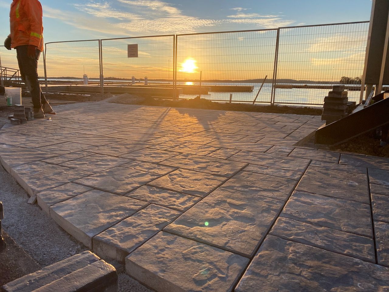 A person is standing on a brick walkway next to a body of water at sunset.