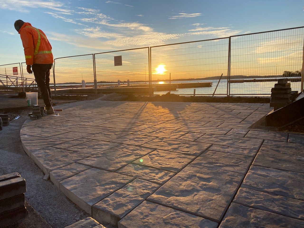 A man is standing on a concrete patio with the sun setting in the background.