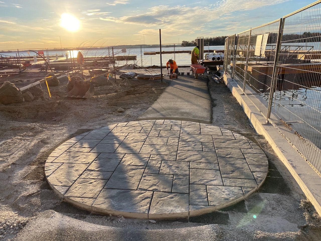 A circular concrete walkway is being built next to a body of water.