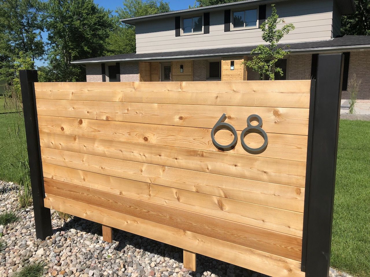 A wooden sign with the number 68 on it is in front of a house.