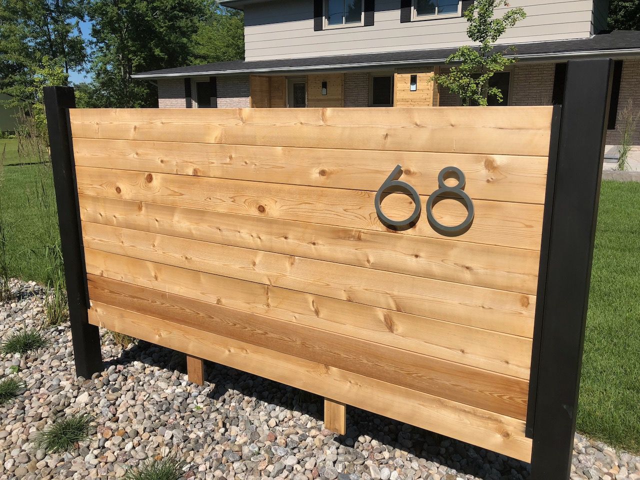 A wooden sign with the number 68 on it is in front of a house.