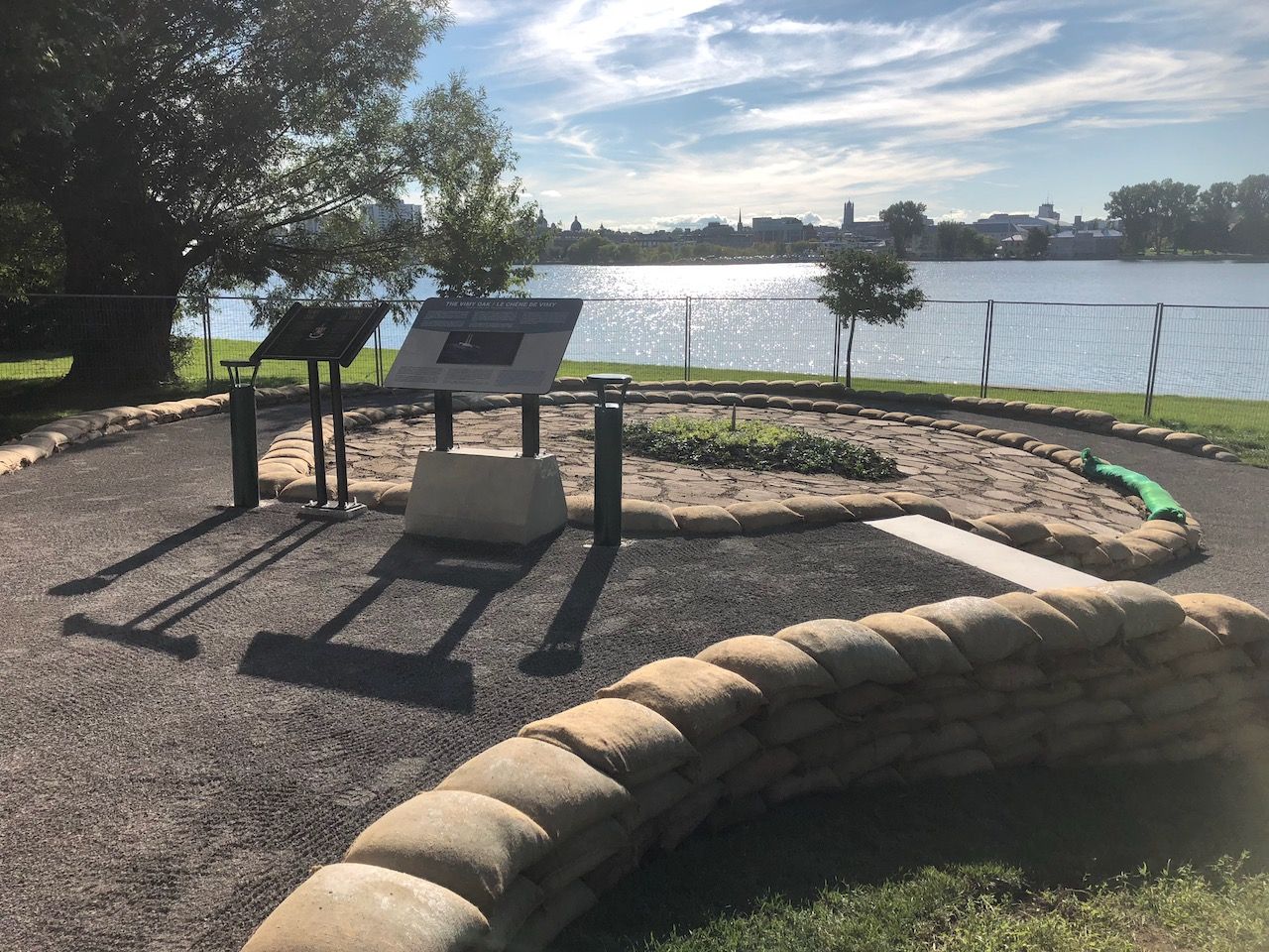 A sandbag wall with a sign in the middle of it and a lake in the background.
