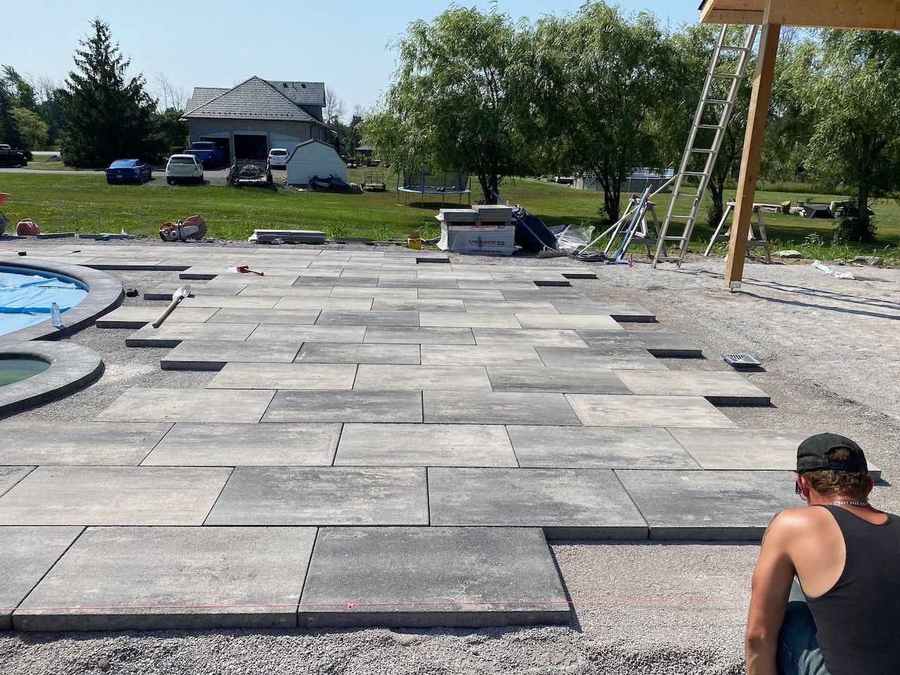 A man is sitting on a concrete patio next to a pool.